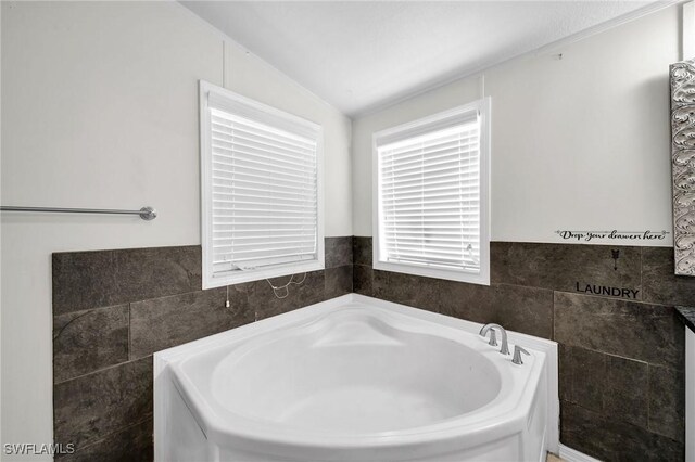 bathroom featuring tile walls, lofted ceiling, and a tub