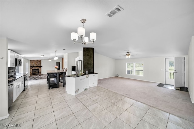 kitchen with stainless steel appliances, ceiling fan with notable chandelier, white cabinets, light carpet, and a stone fireplace