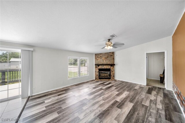 unfurnished living room with a stone fireplace, a textured ceiling, ceiling fan, and hardwood / wood-style floors