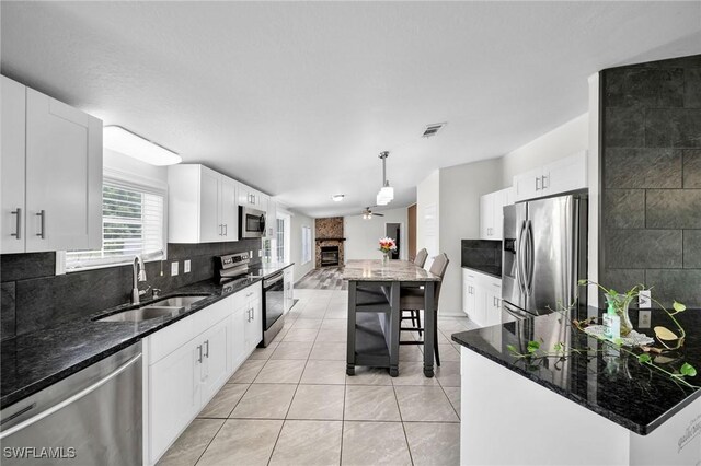 kitchen with dark stone countertops, a center island, stainless steel appliances, pendant lighting, and sink