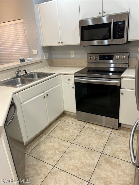 kitchen with stainless steel appliances, sink, white cabinetry, and light tile floors