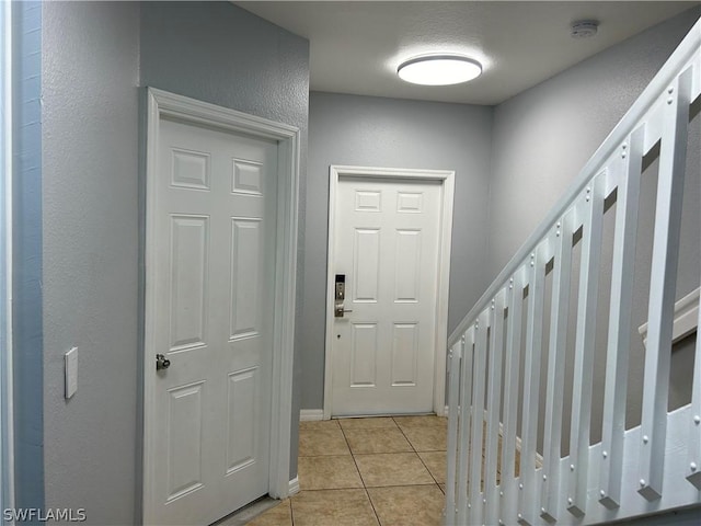 entrance foyer featuring baseboards, a textured wall, light tile patterned floors, and stairway