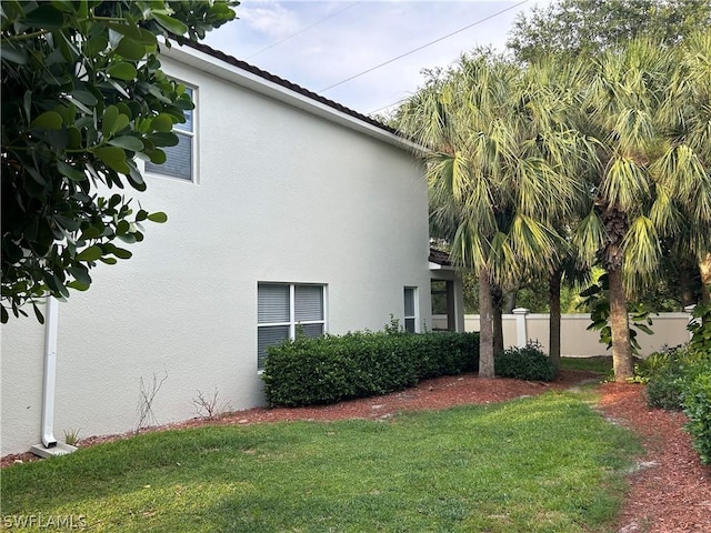 view of side of home with fence, stucco siding, and a lawn