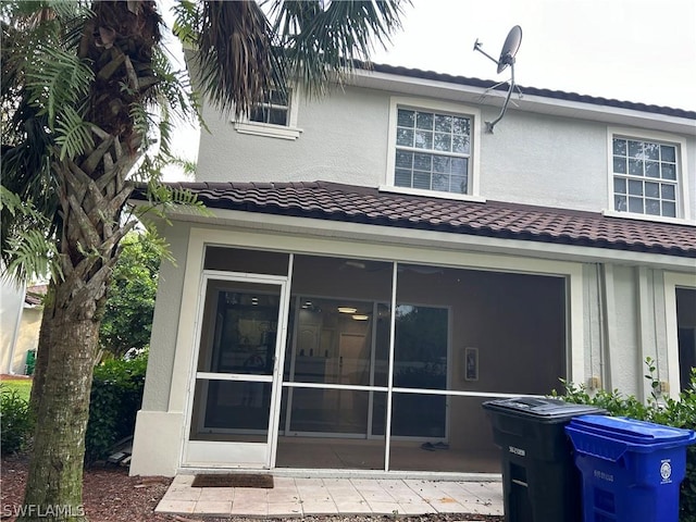 back of house with stucco siding, a sunroom, and a tile roof