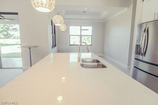 kitchen featuring stainless steel refrigerator with ice dispenser, a raised ceiling, hanging light fixtures, sink, and white cabinetry