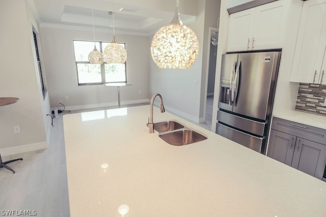 kitchen featuring a tray ceiling, tasteful backsplash, stainless steel refrigerator with ice dispenser, sink, and a chandelier