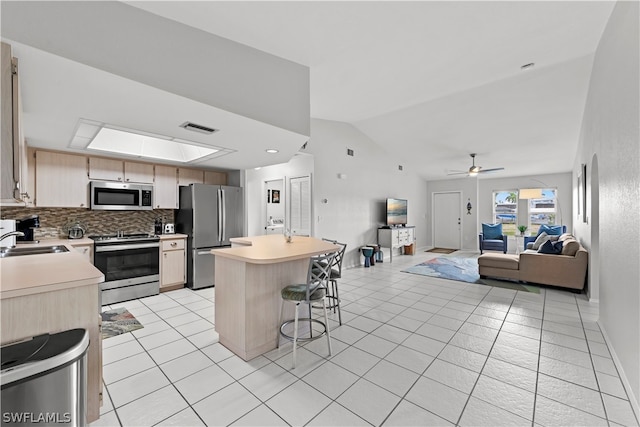 kitchen featuring vaulted ceiling with skylight, stainless steel appliances, ceiling fan, a breakfast bar area, and light tile patterned flooring