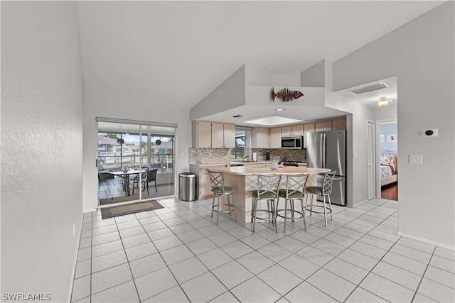 kitchen with a breakfast bar, stainless steel appliances, vaulted ceiling, and light tile patterned flooring