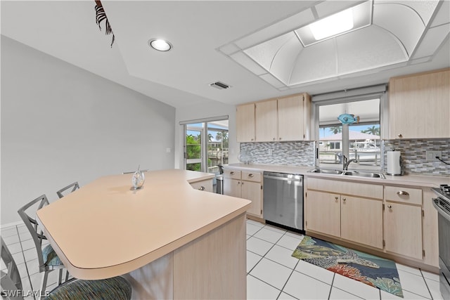 kitchen with appliances with stainless steel finishes, light brown cabinetry, tasteful backsplash, sink, and a breakfast bar area