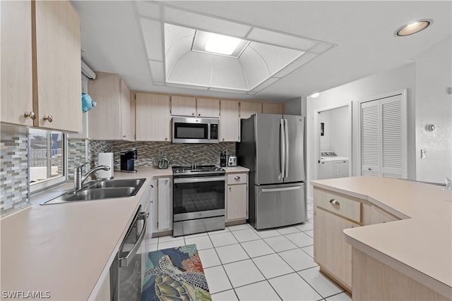 kitchen featuring light brown cabinetry, sink, stainless steel appliances, and washing machine and clothes dryer