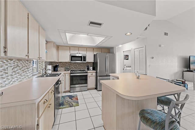 kitchen with sink, lofted ceiling with skylight, stainless steel appliances, and light brown cabinetry