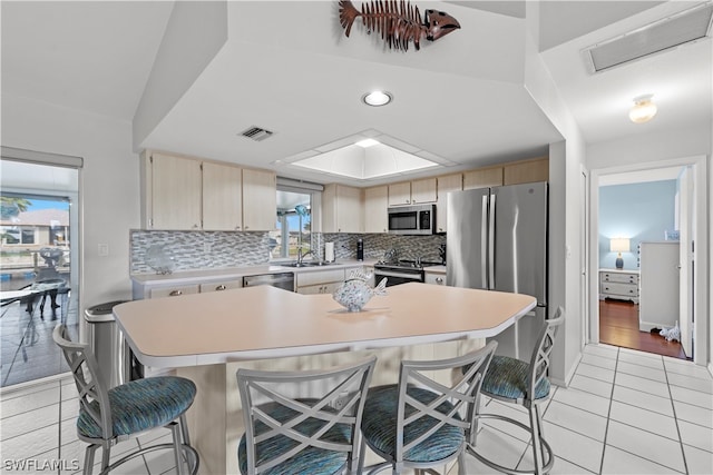 kitchen with a breakfast bar, sink, decorative backsplash, light brown cabinetry, and appliances with stainless steel finishes