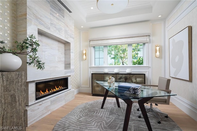 office featuring a raised ceiling, a tile fireplace, light hardwood / wood-style flooring, and ornamental molding