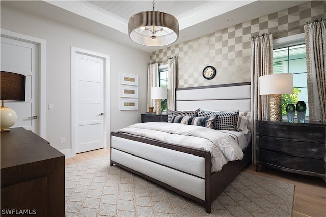 bedroom with a raised ceiling, crown molding, and light hardwood / wood-style flooring