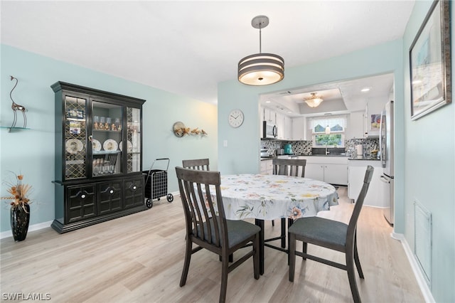 dining room featuring sink, light hardwood / wood-style flooring, and a tray ceiling