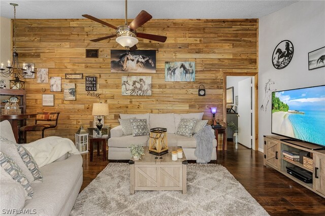 living room featuring a textured ceiling, ceiling fan with notable chandelier, dark hardwood / wood-style floors, and wooden walls