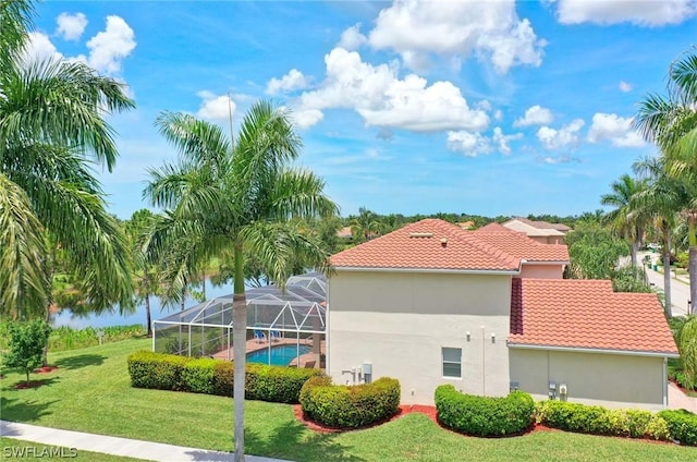 view of home's exterior with a lawn, glass enclosure, and a water view