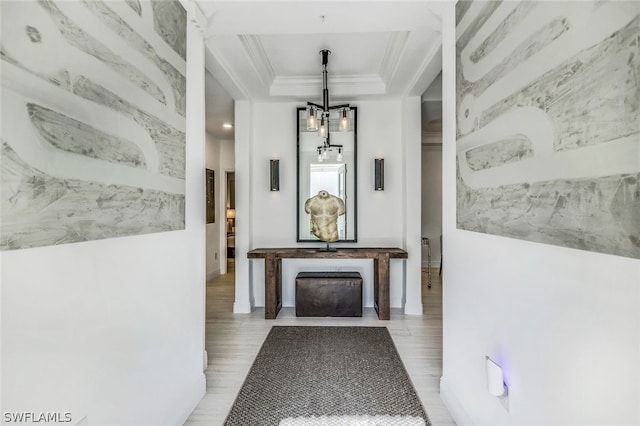 corridor featuring a notable chandelier, light hardwood / wood-style floors, crown molding, and a tray ceiling