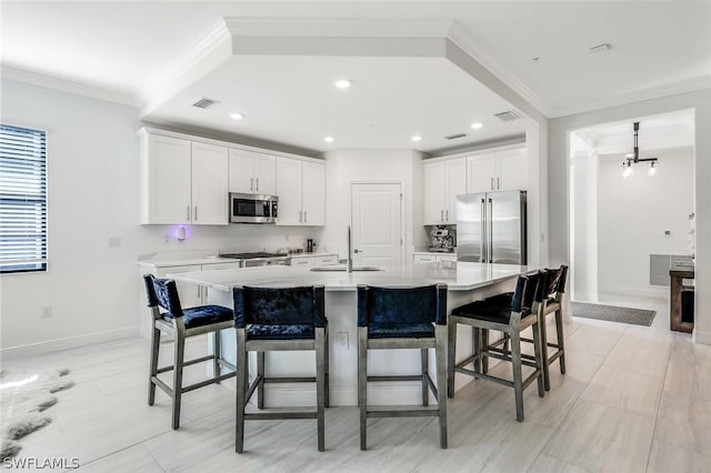 kitchen featuring a kitchen bar, appliances with stainless steel finishes, crown molding, white cabinetry, and a large island