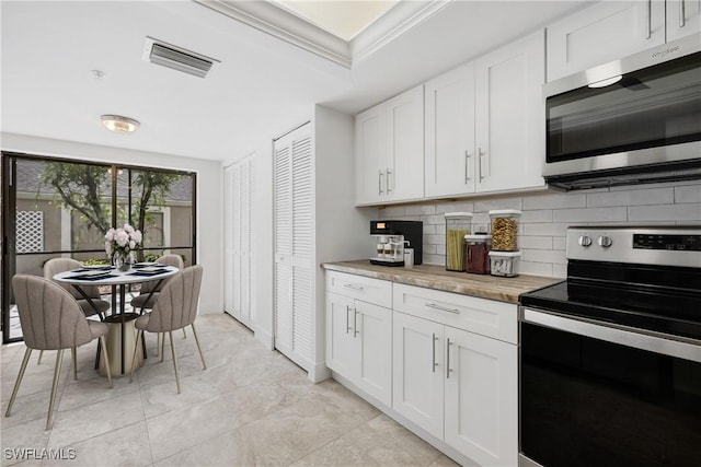 kitchen with white cabinetry, ornamental molding, stainless steel appliances, and backsplash