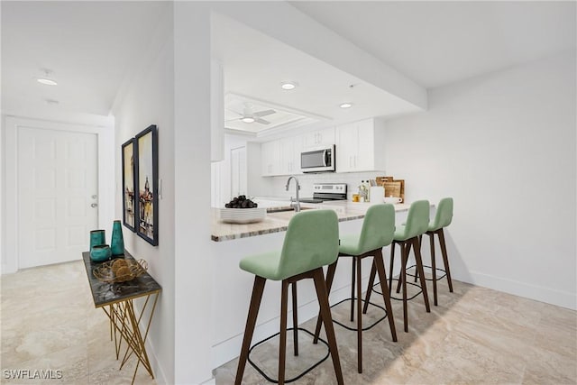 kitchen with a kitchen bar, tasteful backsplash, appliances with stainless steel finishes, kitchen peninsula, and white cabinets