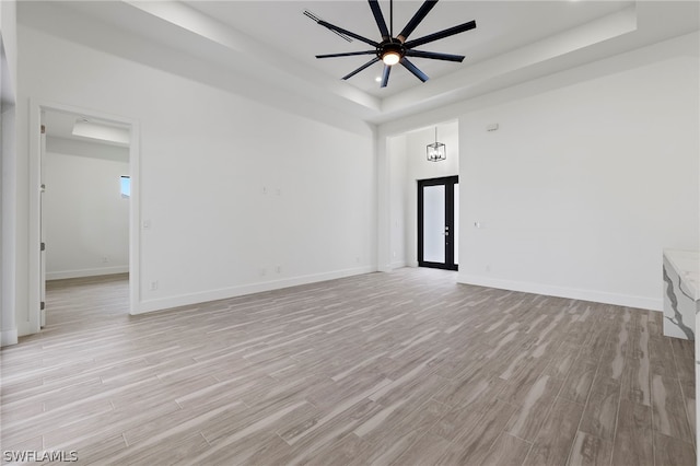 empty room featuring ceiling fan, a tray ceiling, and light wood-type flooring