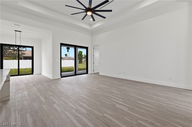 unfurnished room with ceiling fan, a high ceiling, light hardwood / wood-style floors, and a raised ceiling