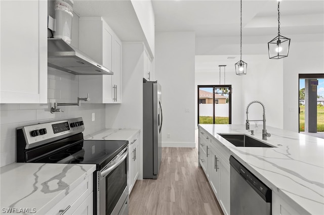 kitchen featuring decorative light fixtures, wall chimney range hood, light hardwood / wood-style floors, a healthy amount of sunlight, and appliances with stainless steel finishes