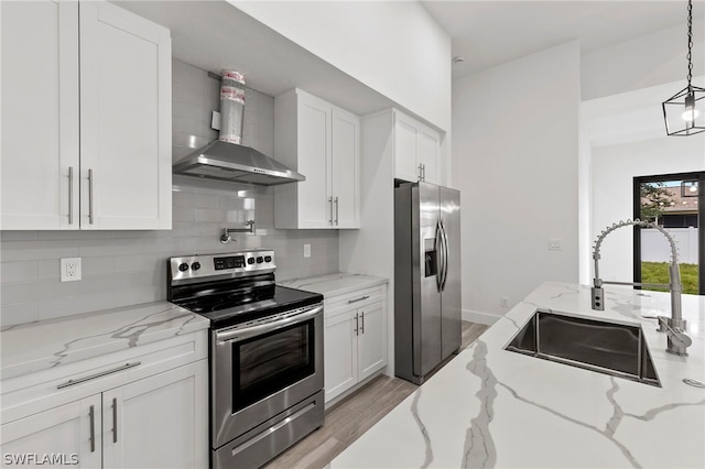 kitchen with light stone counters, light hardwood / wood-style floors, stainless steel appliances, wall chimney exhaust hood, and white cabinets