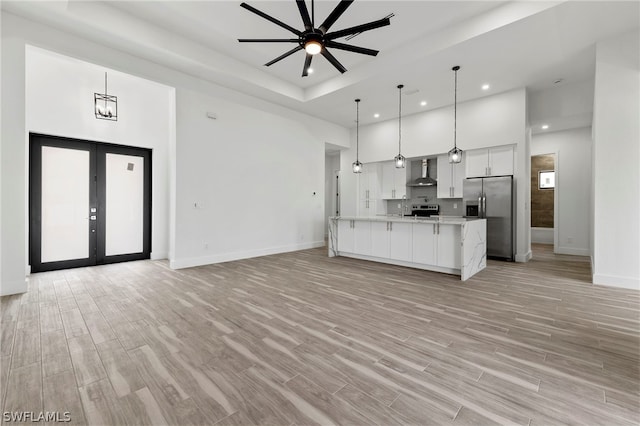 kitchen featuring wall chimney range hood, french doors, hanging light fixtures, stainless steel appliances, and ceiling fan