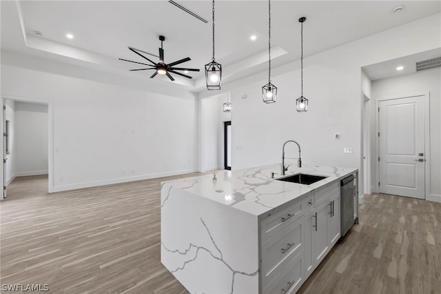 kitchen featuring decorative light fixtures, a center island with sink, light hardwood / wood-style flooring, and a raised ceiling