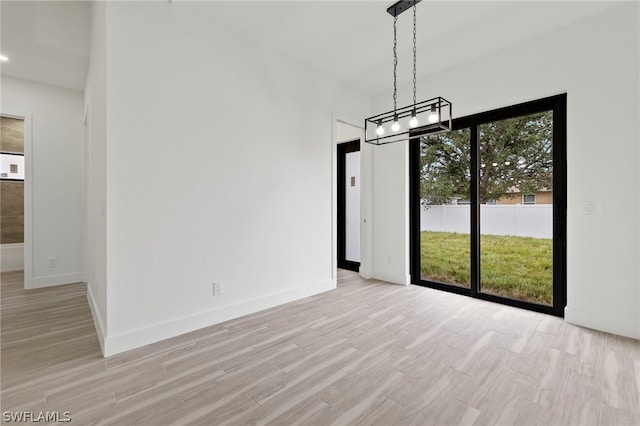 unfurnished dining area with a notable chandelier, a wealth of natural light, and light wood-type flooring