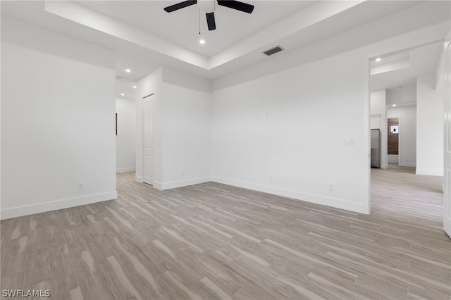 empty room featuring ceiling fan, light wood-type flooring, and a raised ceiling