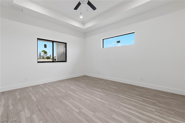 spare room featuring a tray ceiling, ceiling fan, and light hardwood / wood-style floors