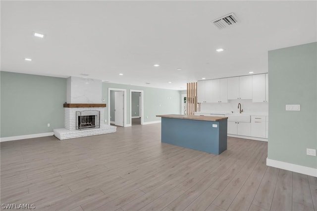 kitchen with light hardwood / wood-style flooring, sink, white cabinets, a fireplace, and a center island