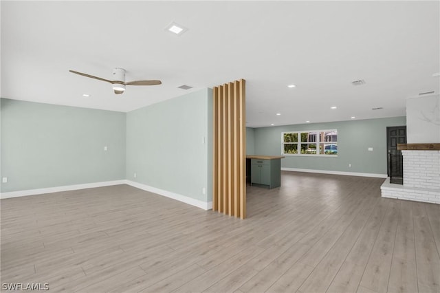 unfurnished living room with ceiling fan, a brick fireplace, and light hardwood / wood-style flooring