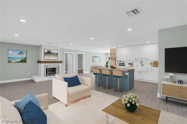 living area with light wood-style floors, recessed lighting, a brick fireplace, and visible vents