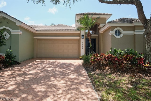 view of front of property featuring decorative driveway, an attached garage, a tile roof, and stucco siding