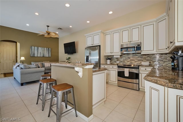 kitchen with a center island, stainless steel appliances, light tile patterned floors, dark stone counters, and ceiling fan