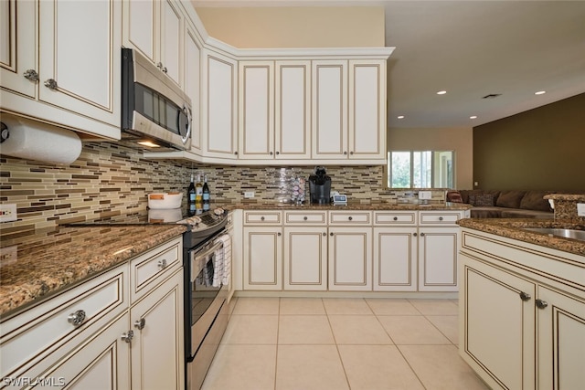 kitchen with appliances with stainless steel finishes, stone counters, light tile patterned floors, decorative backsplash, and sink