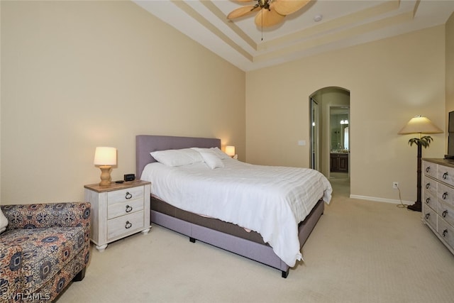 carpeted bedroom with ensuite bathroom, ceiling fan, and a tray ceiling