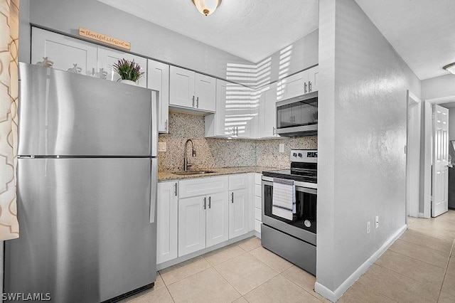 kitchen with sink, light stone countertops, appliances with stainless steel finishes, light tile patterned flooring, and white cabinetry