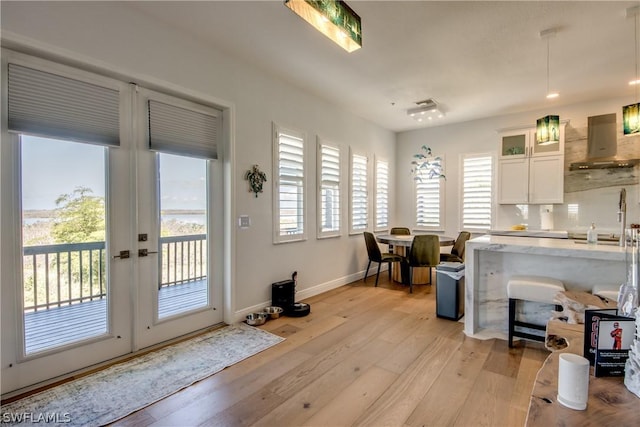 interior space featuring wall chimney range hood, light hardwood / wood-style flooring, white cabinets, decorative light fixtures, and french doors