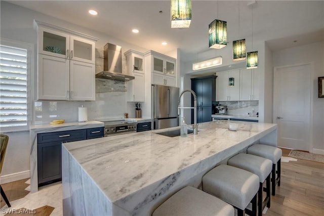 kitchen featuring wall chimney range hood, a center island with sink, stainless steel appliances, and backsplash