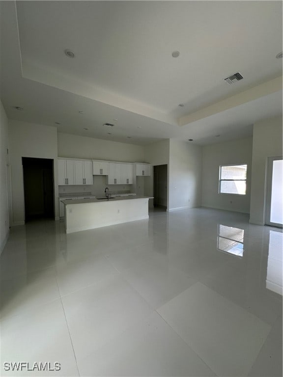 unfurnished living room with a raised ceiling, sink, and light tile patterned flooring