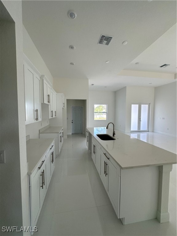 kitchen featuring white cabinetry, sink, light stone counters, a large island with sink, and light tile patterned floors