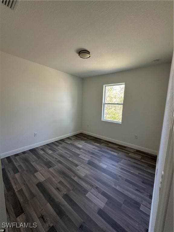 empty room with dark wood-style floors, visible vents, and baseboards