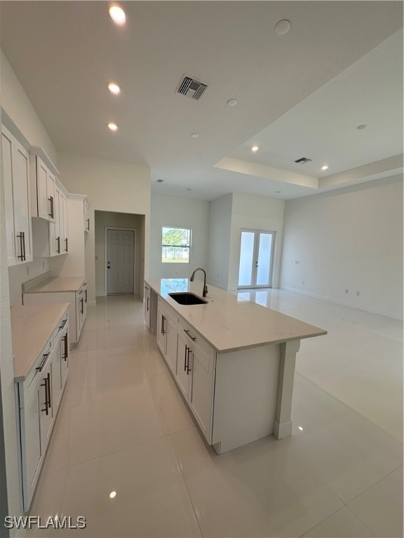 kitchen with a large island with sink, light stone counters, sink, and white cabinets