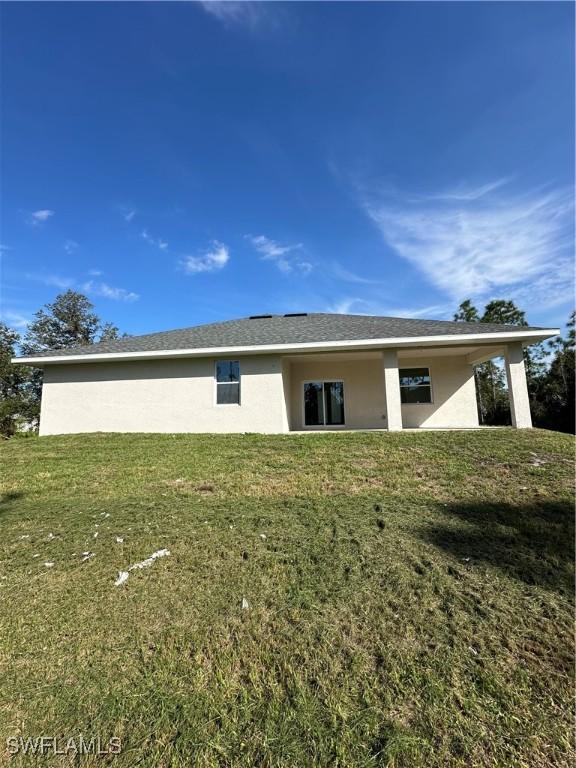 back of property with stucco siding and a yard