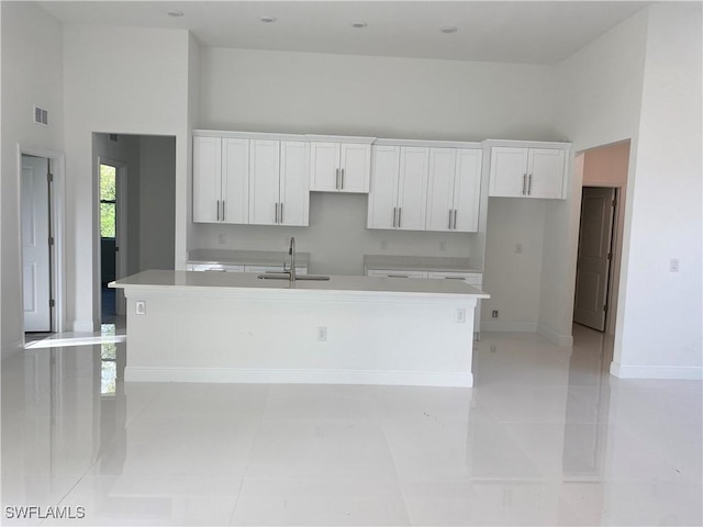 kitchen with a towering ceiling, a kitchen island with sink, white cabinets, and a sink